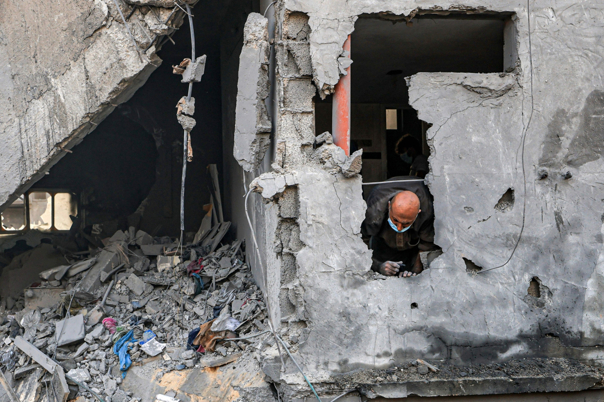 2023年10月25日，加薩走廊南部的甘尤尼斯（Khan Yunis）遭以色列轟炸，民眾在倒塌的建築物尋找生還者和受害者遺體時，一名男子從牆上的洞向外望。©MAHMUD HAMS/AFP via Getty Images