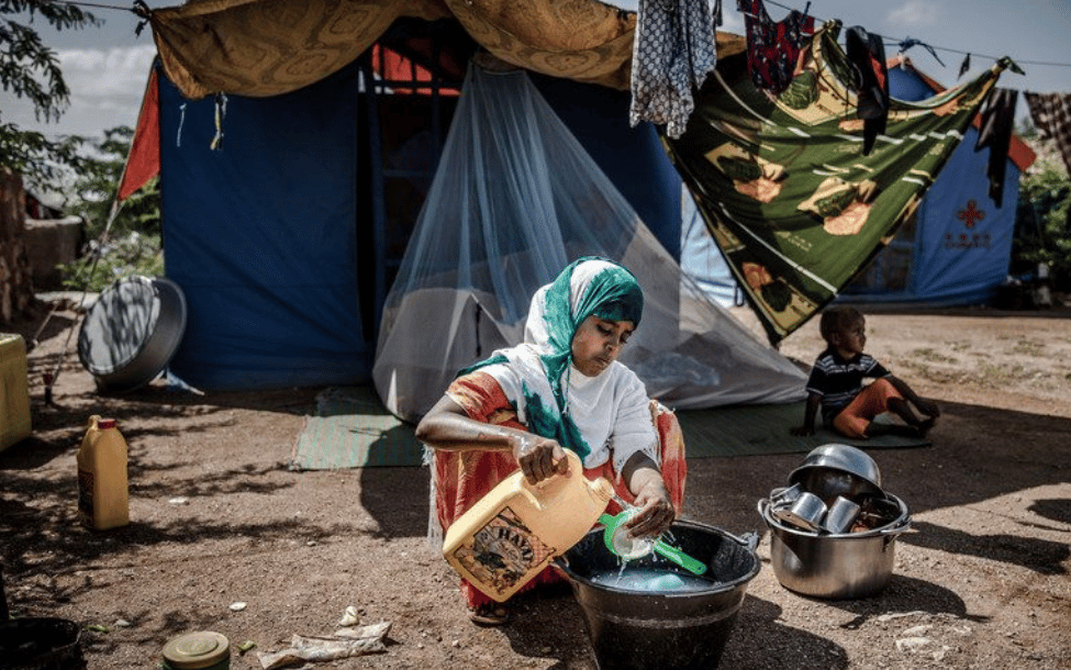 一名年輕女子與一名兒童在索馬利亞貝萊德韋內地區（ Beledweyne, Somalia），因豪雨而流離失所，坐在帳篷外洗碗。氣候變遷帶來的洪水與乾旱循環，使索馬利亞數十萬人陷入脆弱處境並被迫流離失所。
