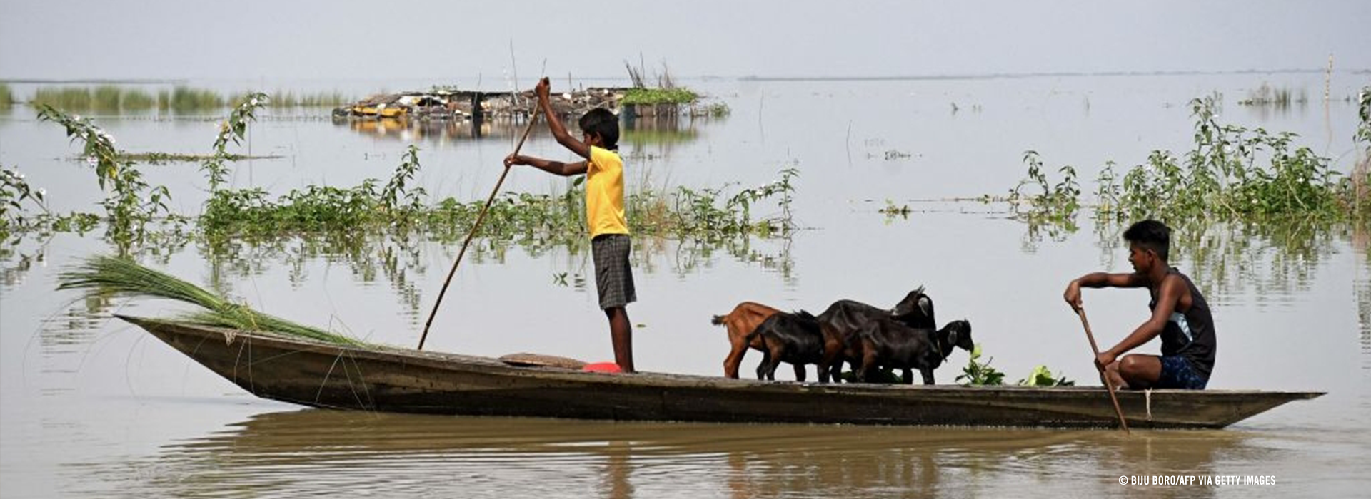 2023年8月印度阿薩姆邦（Assam）洪災過後，兩名男童帶著家當乘船。© Biju Boro/AFP via Getty Images